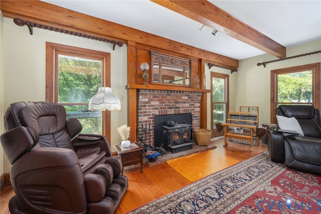 Wood-finish flooring with exposed wood beams, a brick fireplace with a wood-burning stove insert, and wood window trim