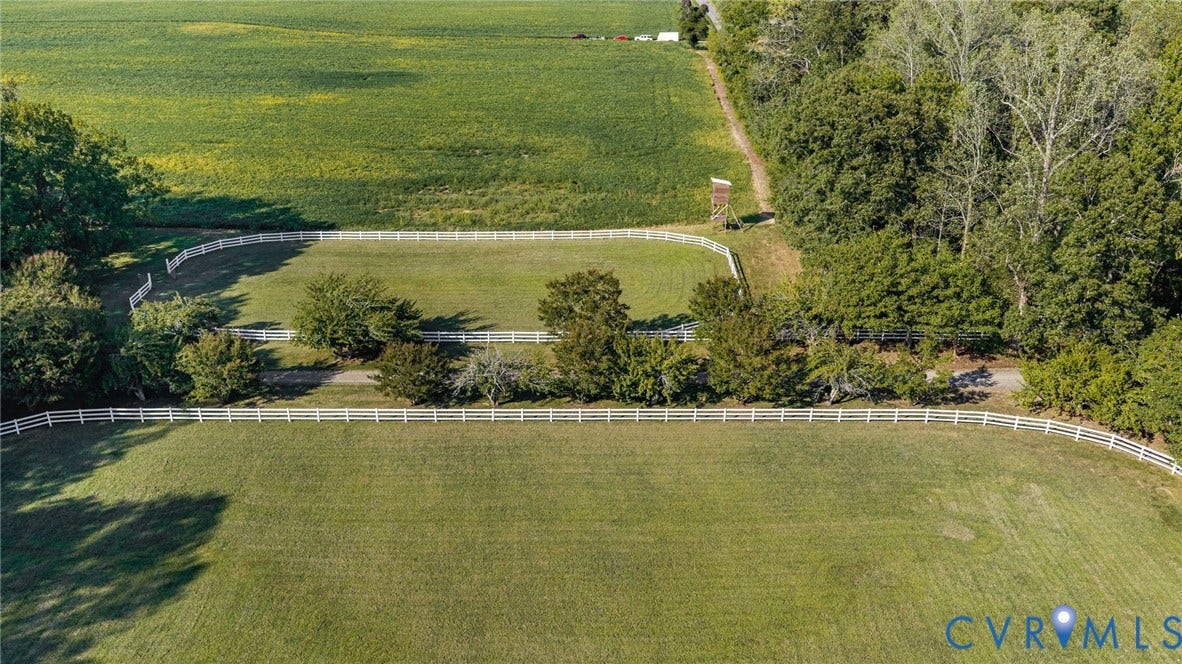 Expansive green pastures with white fencing, bordered by mature trees and additional cultivated land