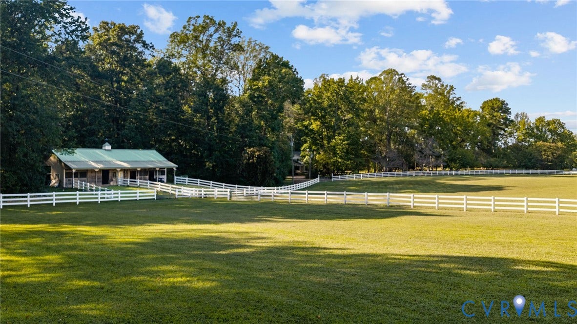 Expansive green lawn with white fencing, mature trees, and a barn-style outbuilding featuring a green metal roof and covered porch