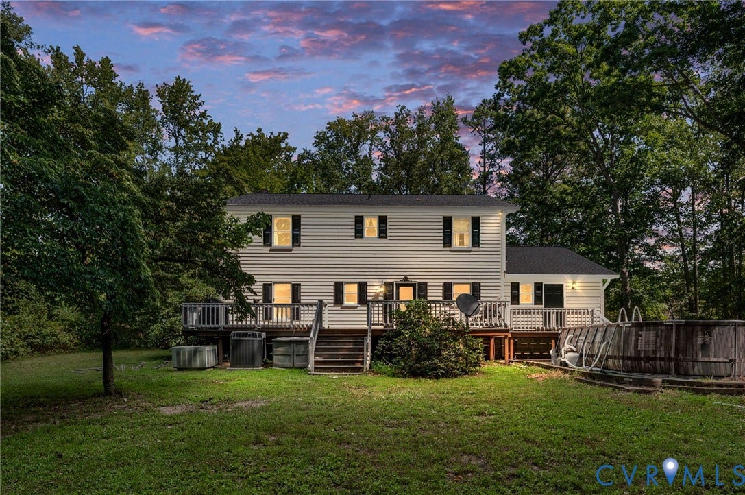Two-story residence with white siding and black shutters, featuring a multi-level wood deck and an above-ground pool