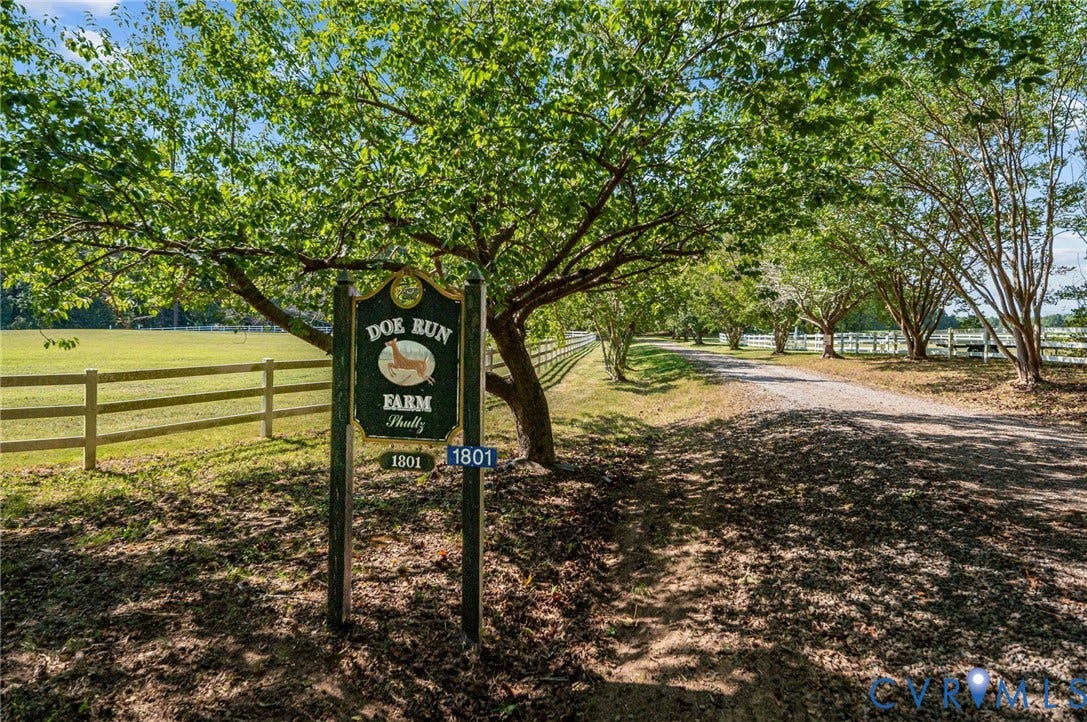 Gravel drive leading to the property, bordered by mature trees and a manicured lawn with a white fence