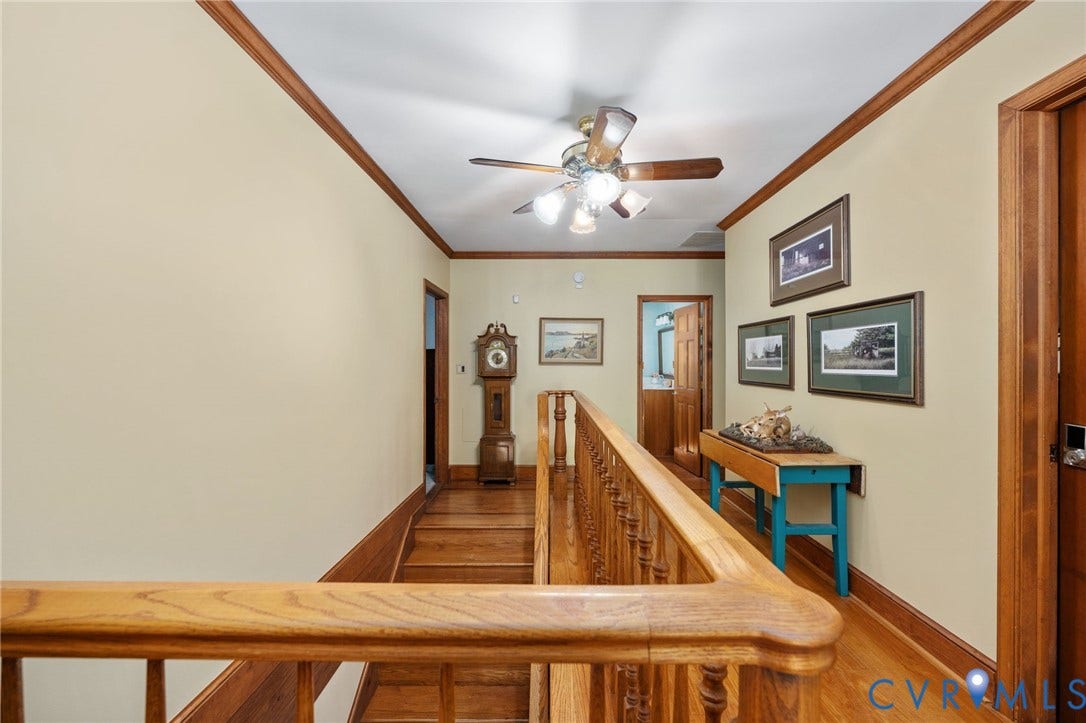 Hardwood flooring, wood trim details, wood banister, and a ceiling fan with light fixture