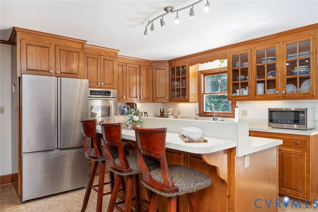Wood-finish cabinetry with glass-front display cabinets, stainless steel appliances, track lighting, and a kitchen island with seating