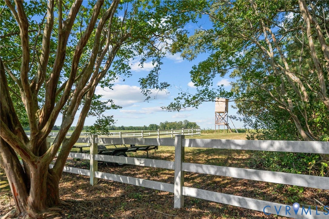 Expansive outdoor space featuring a white multi-rail fence and mature trees