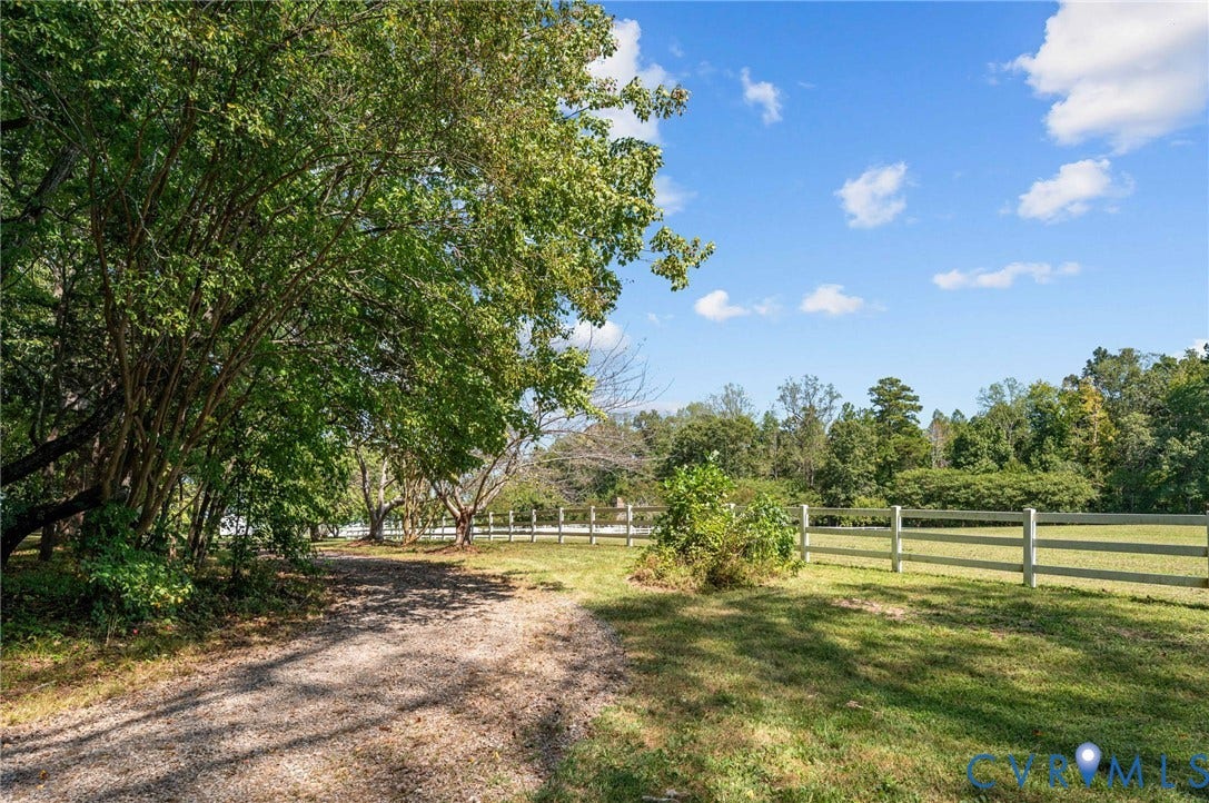 Expansive green space with mature trees, a gravel pathway, and a white rail fence