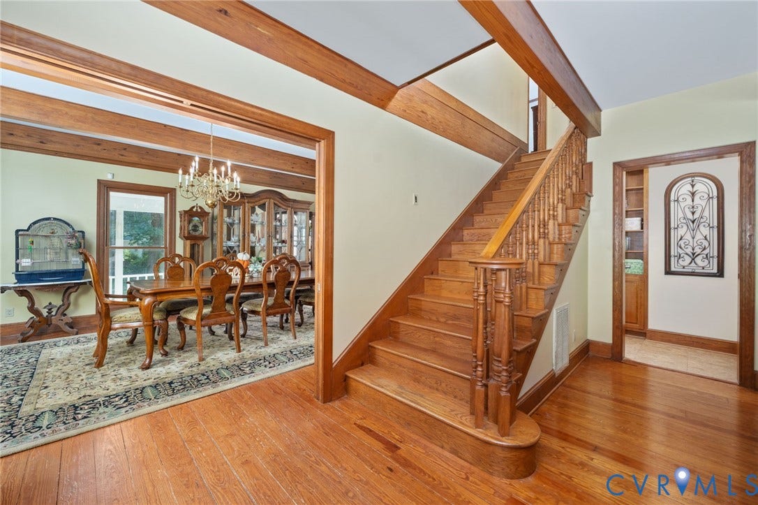 Hardwood flooring throughout, exposed wood beams, wood staircase with ornate balusters, and a formal dining space with a chandelier