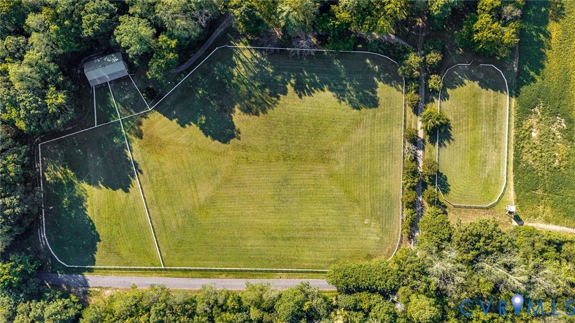 Expansive green acreage featuring multiple fenced paddocks, surrounding mature trees, and a shaded outbuilding