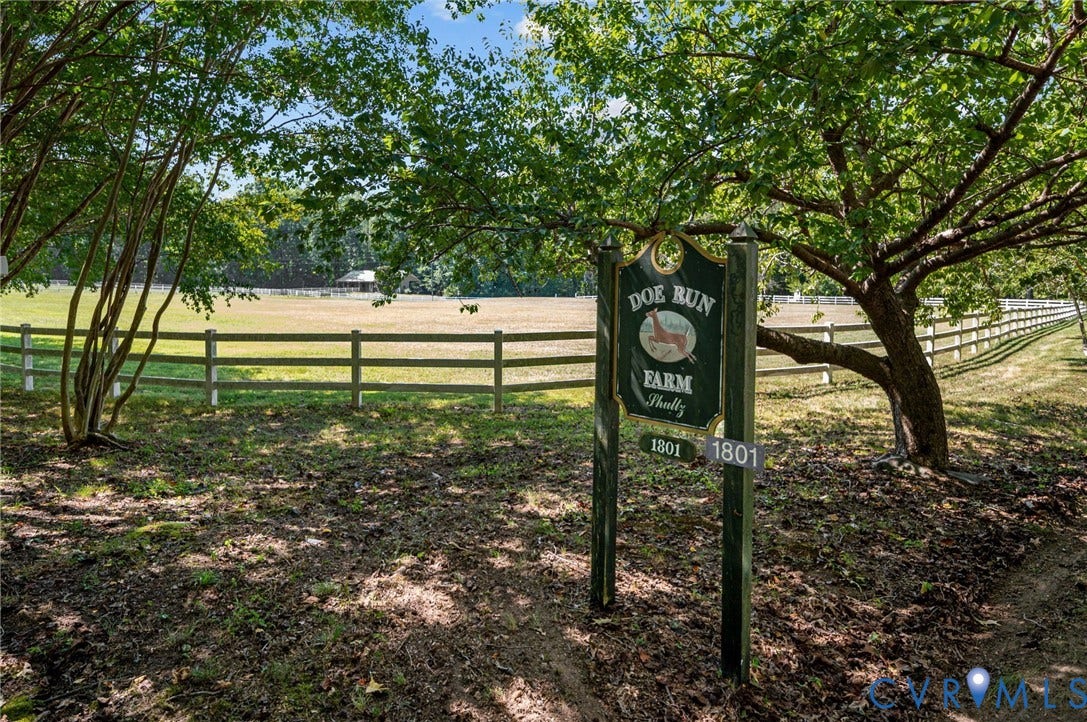 Gated property entrance featuring mature trees and a wooden fence bordering expansive acreage