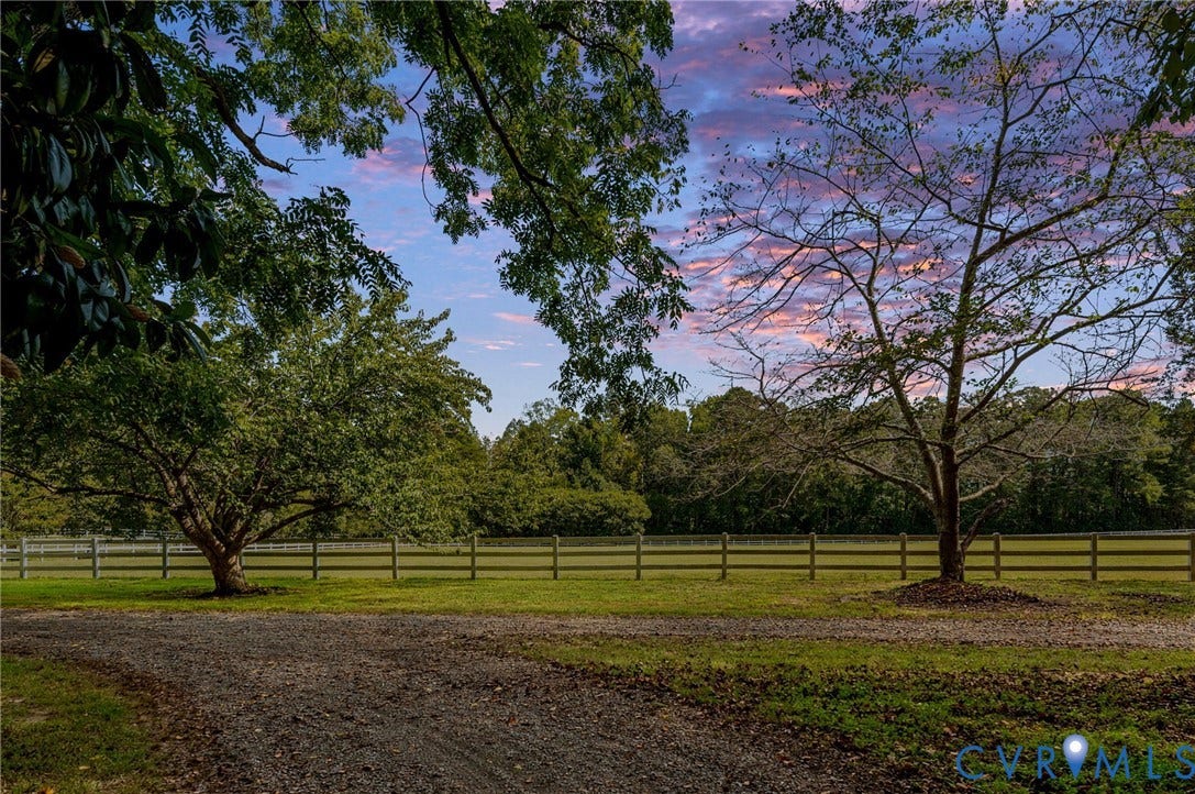 Gravel driveway leading to a fenced pasture with mature trees