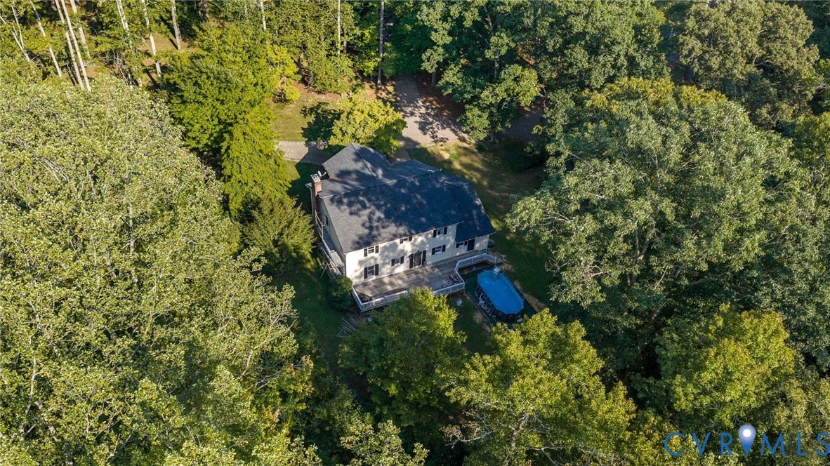 Two-story residential structure featuring multiple dormer windows, a dark shingled roof, a paved driveway, and surrounded by mature trees