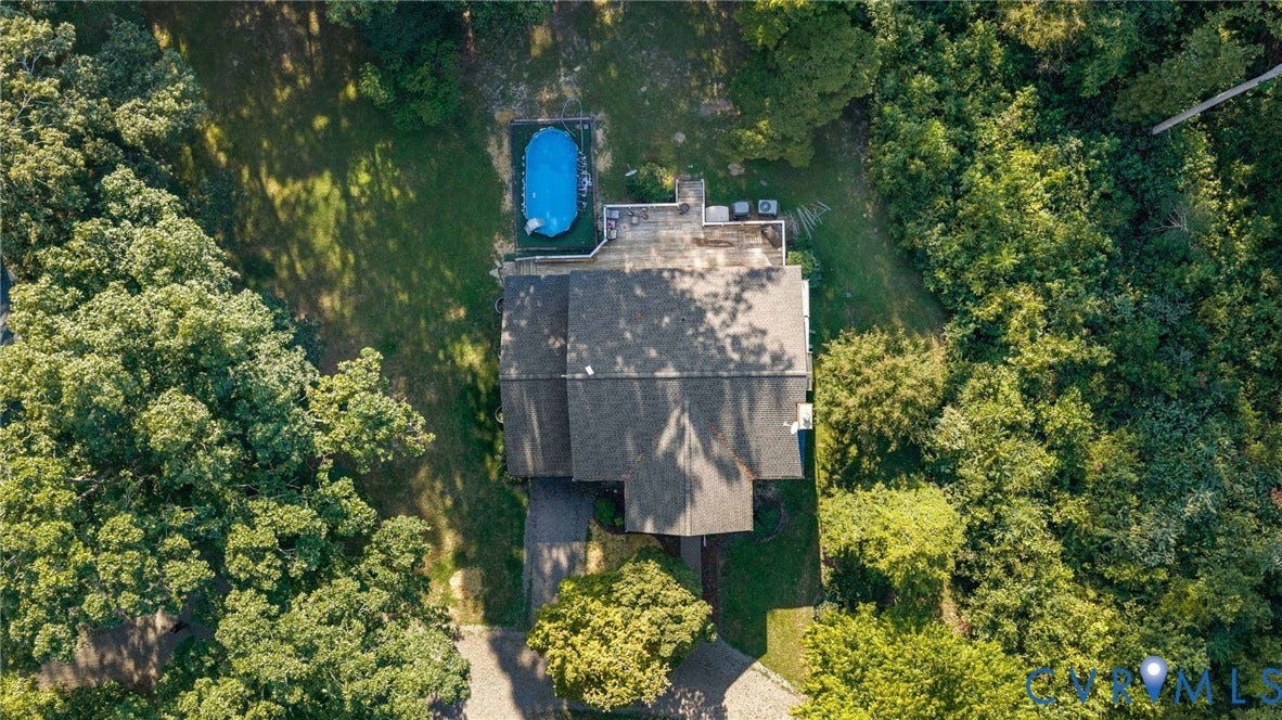 Expansive lot with a large residential structure, surrounding mature trees, a swimming pool, and a paved driveway