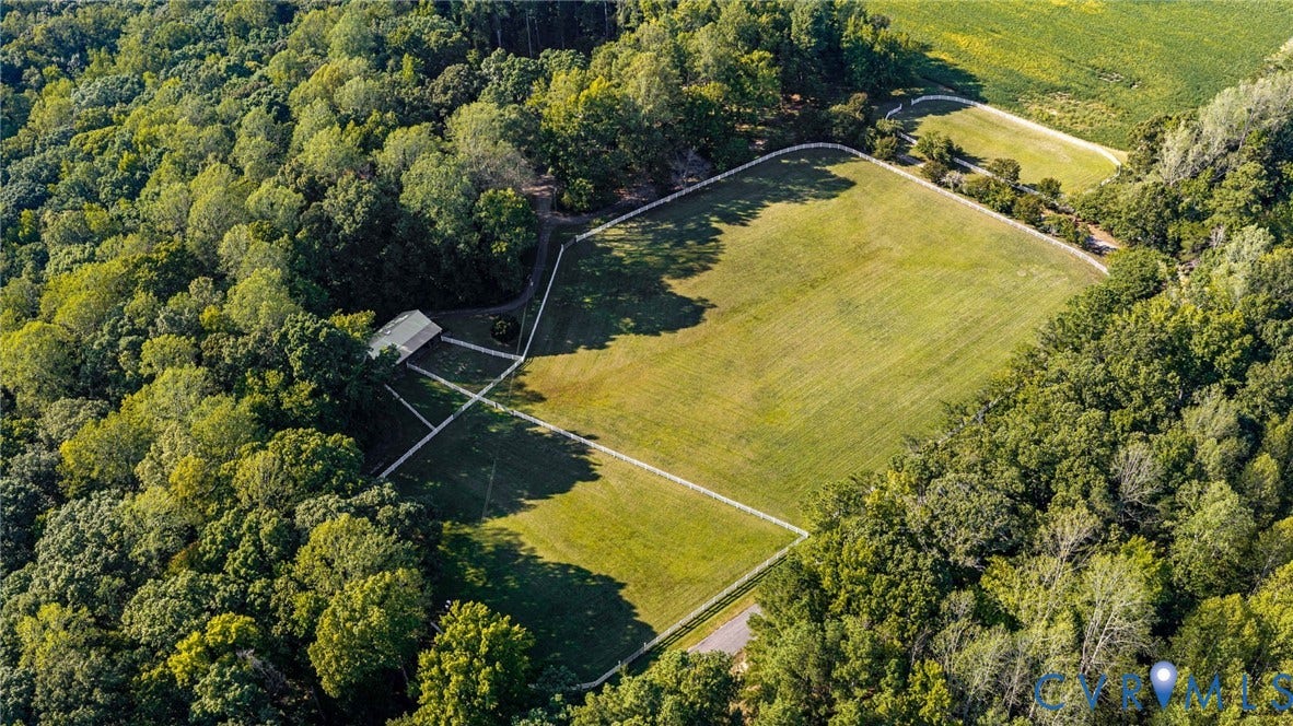 Expansive green acreage featuring a large open field, surrounded by dense mature trees, and a visible outbuilding