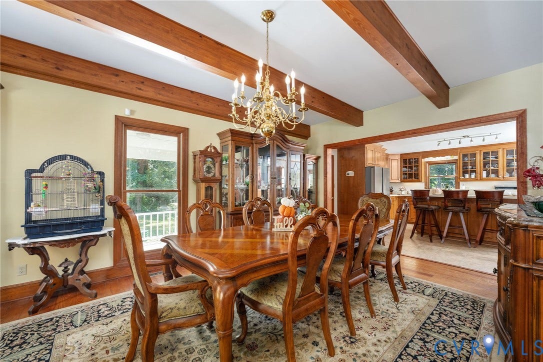 Hardwood flooring, exposed wood ceiling beams, a brass chandelier, and wood-trimmed window