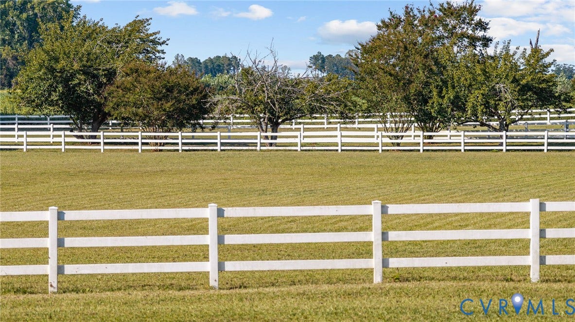 Expansive green pasture framed by white fencing and mature trees