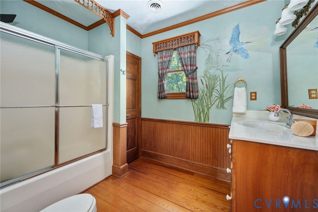 Bathtub with sliding glass enclosure, wood-finish flooring, wood vanity with integrated sink, and wood wainscoting