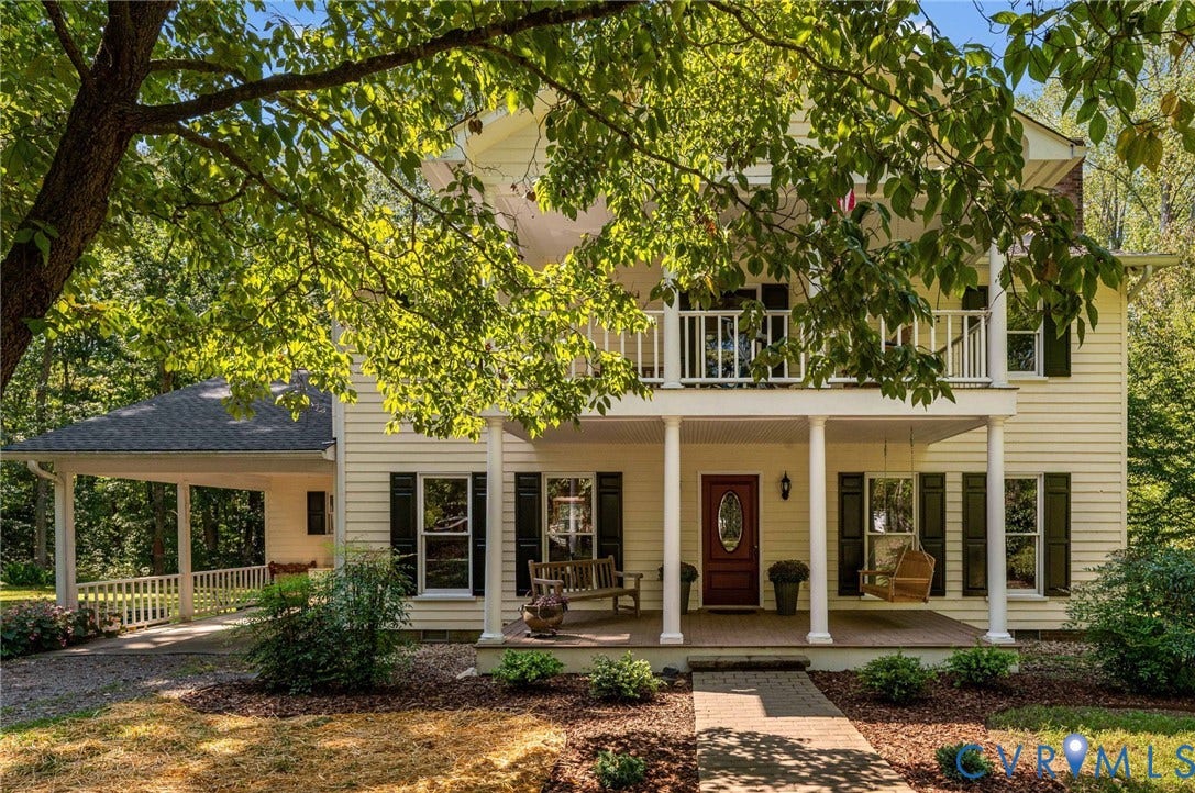Two-story residence featuring a covered front porch, an upper-level balcony, a covered carport, and a stone walkway