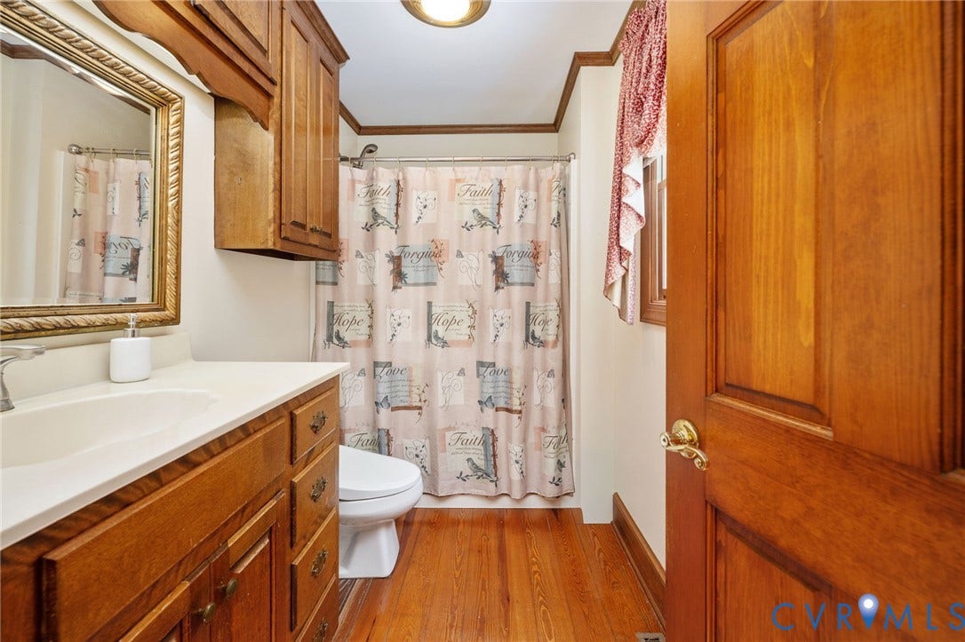 Wood-finish flooring, wood-finish vanity with countertop and integrated sink, wall-mounted wood-finish cabinetry, and a framed mirror
