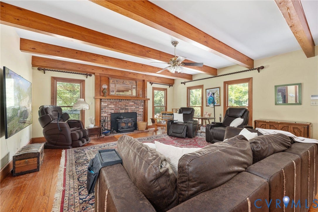 Exposed wood beam ceiling, brick fireplace with wood stove, wood-frame windows, and wood-finish flooring