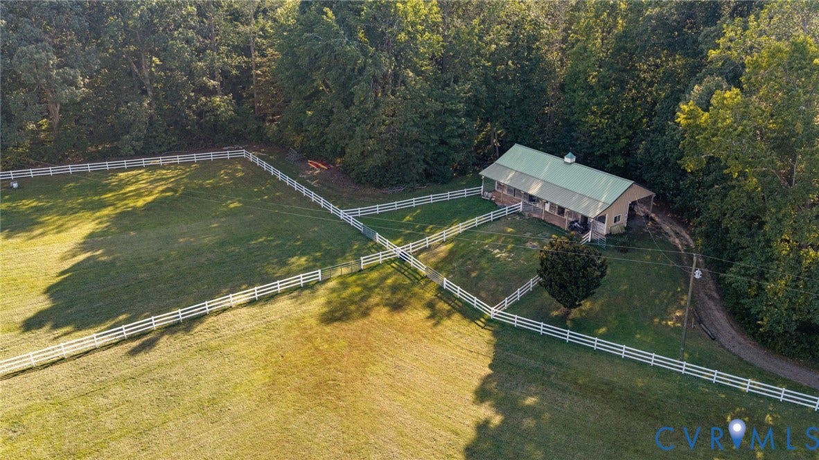 Expansive fenced pastures, detached barn structure with a green metal roof, surrounded by mature trees, and a gravel driveway