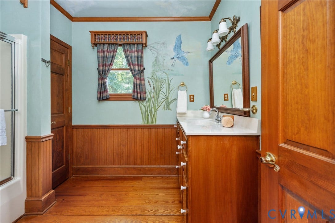 Wood-finish flooring, wood-paneled walls, wood vanity with integrated sink, rectangular mirror, and shower enclosure