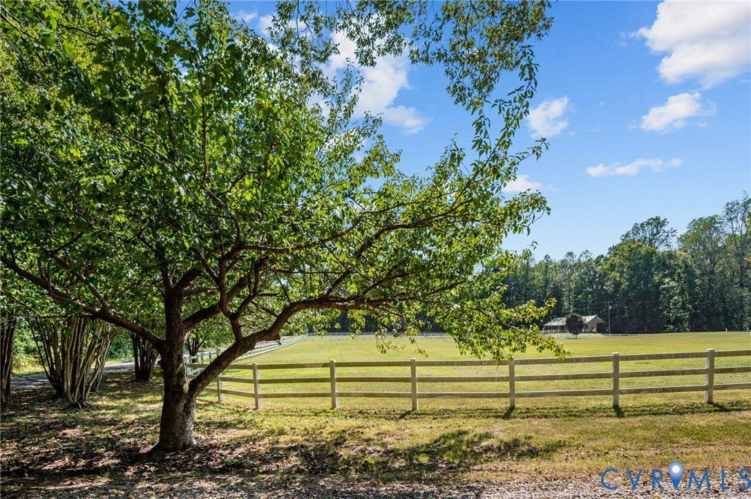 Expansive fenced pasture with lush green grass and mature trees