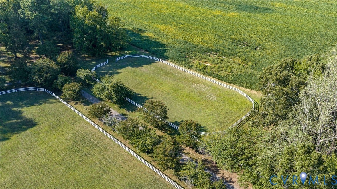 Expansive green acreage featuring white fencing, mature trees, and a gravel pathway