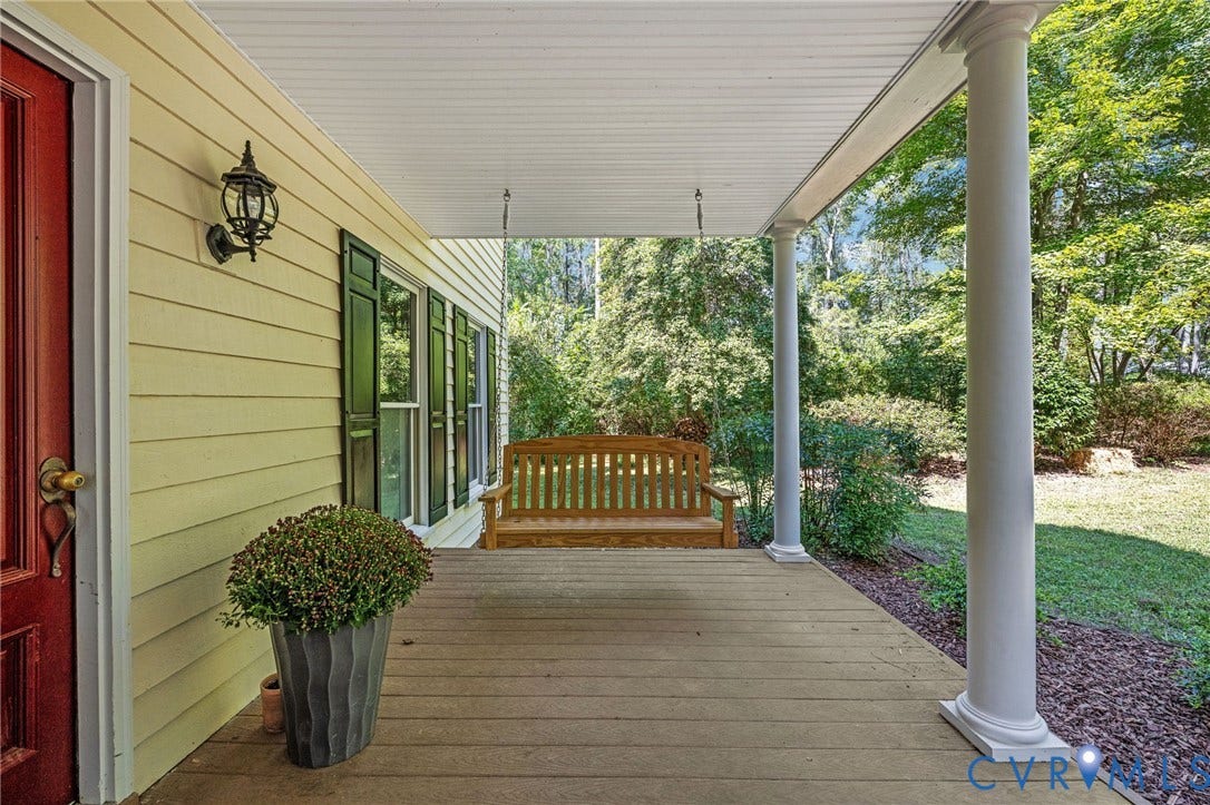 Covered front porch featuring wood-finish decking, decorative white columns, and horizontal siding