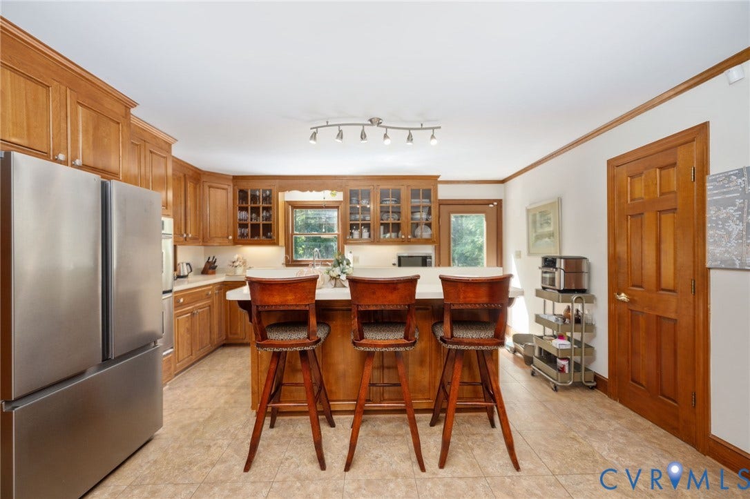 Stainless steel refrigerator, wood-finish cabinetry, built-in kitchen island, track lighting fixture, and tile flooring