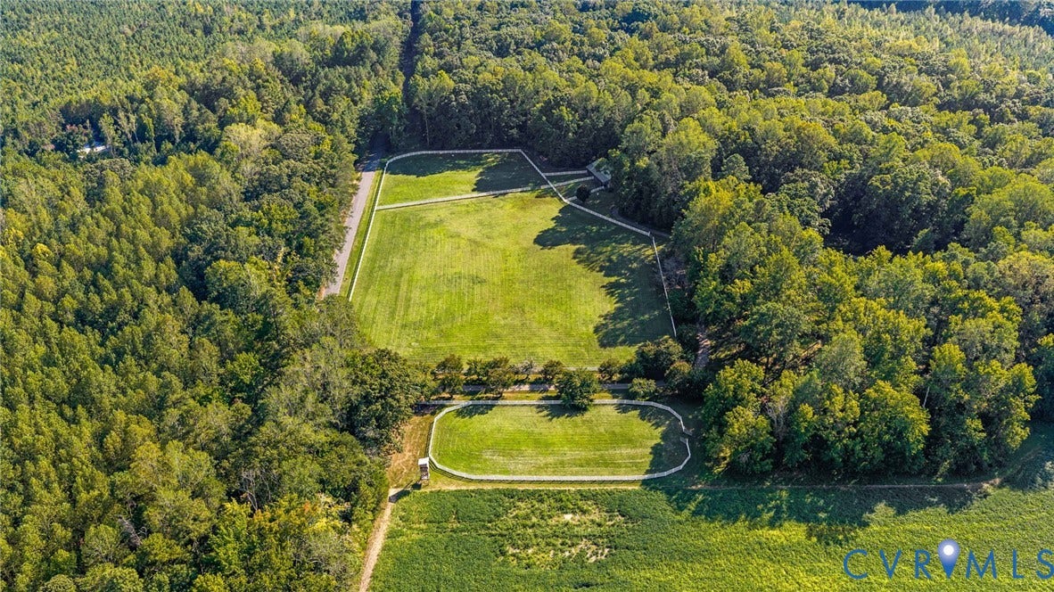 Expansive acreage featuring multiple fenced paddocks, surrounding mature tree lines, and open fields