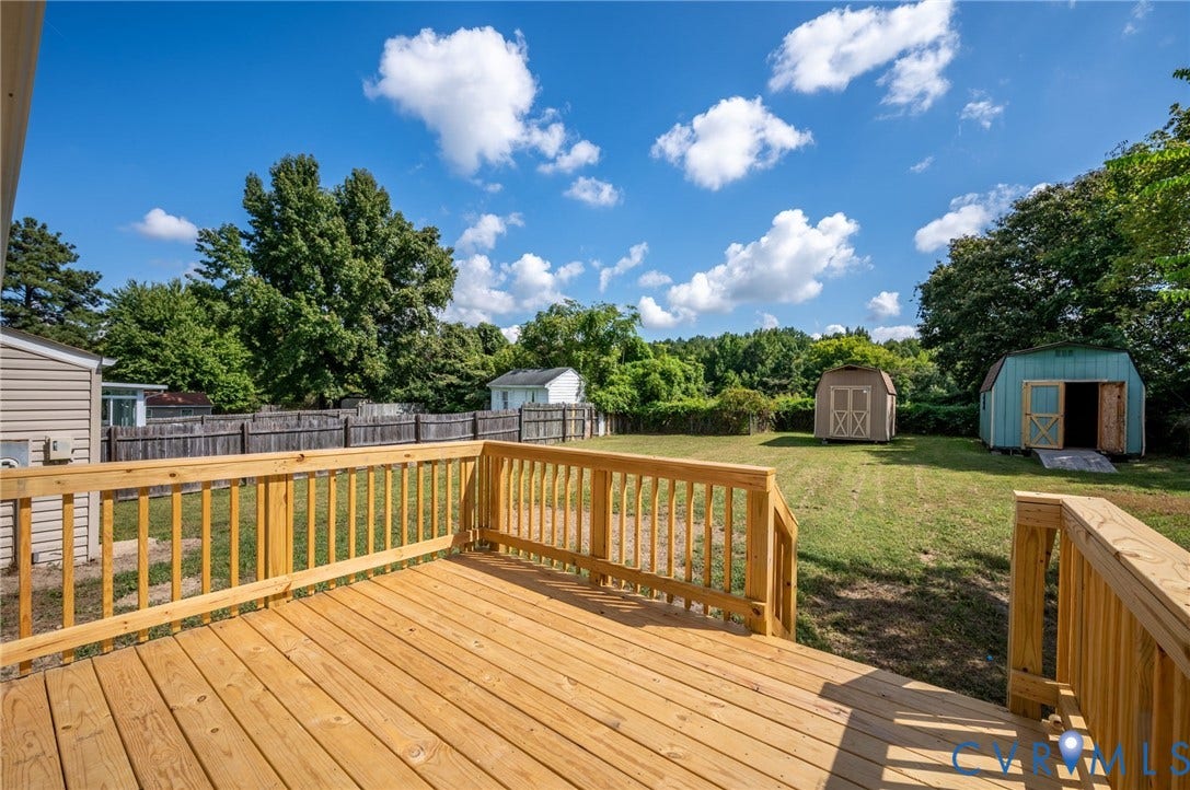 4411 Samara Drive, Henrico, VA 23231 Expansive wood deck with natural wood railing, overlooking a fenced backyard with a manicured lawn, and two detached storage sheds