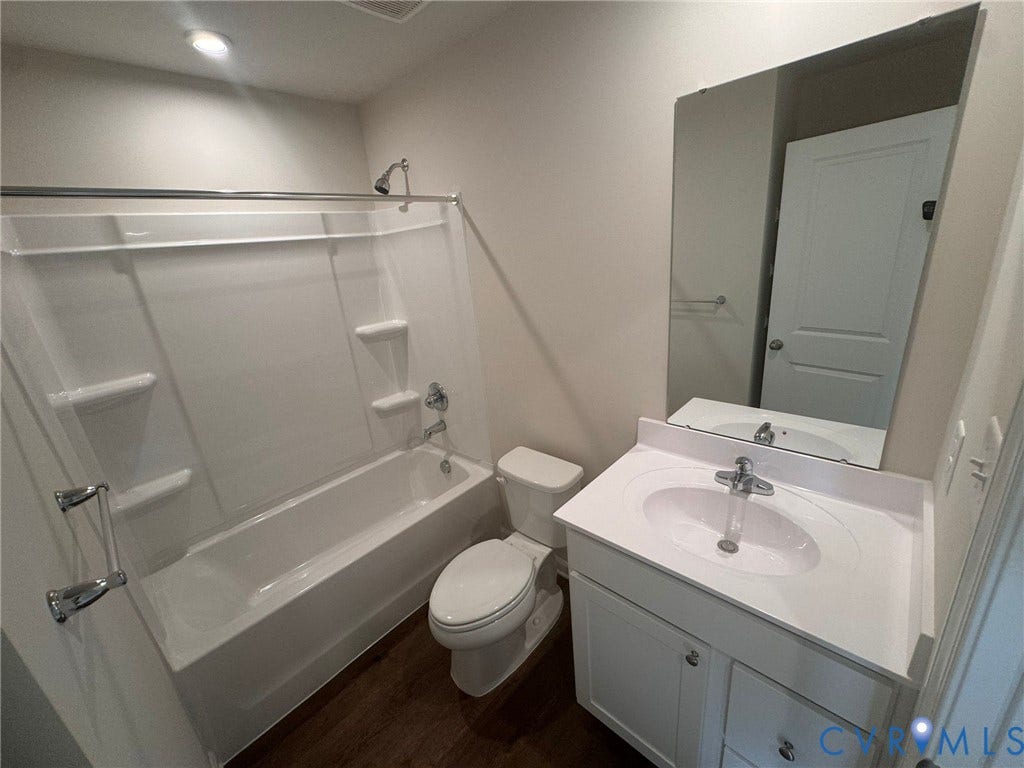 White vanity with integrated sink, chrome faucet, wall-mounted mirror, and wood-finish flooring