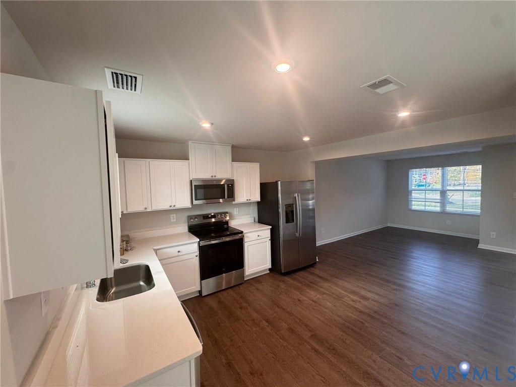 Kitchen featuring white shaker cabinetry, stainless steel appliances, light-toned countertops, and wood-finish flooring