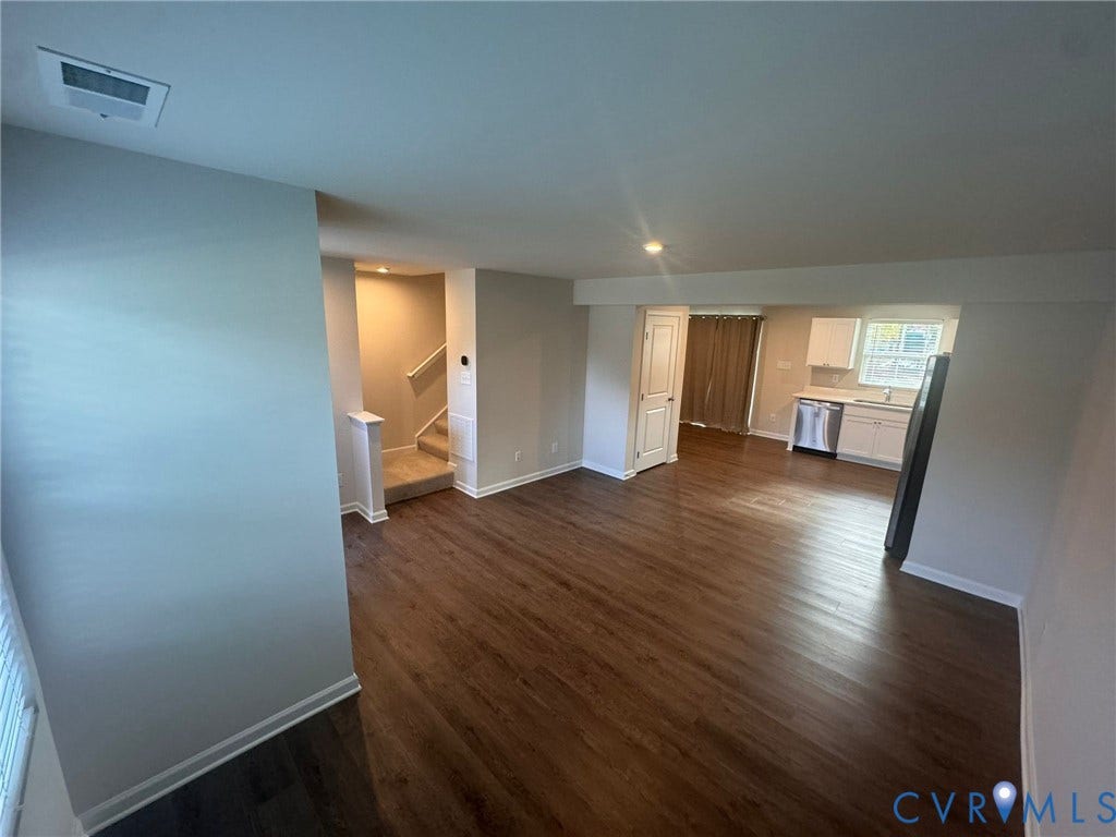Hardwood-finish flooring, white painted walls, recessed lighting, and a partial view of a kitchen with white cabinetry and stainless steel appliances