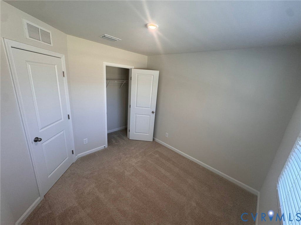 Carpeted flooring, white interior doors with dark hardware, recessed ceiling lighting, and a window with blinds