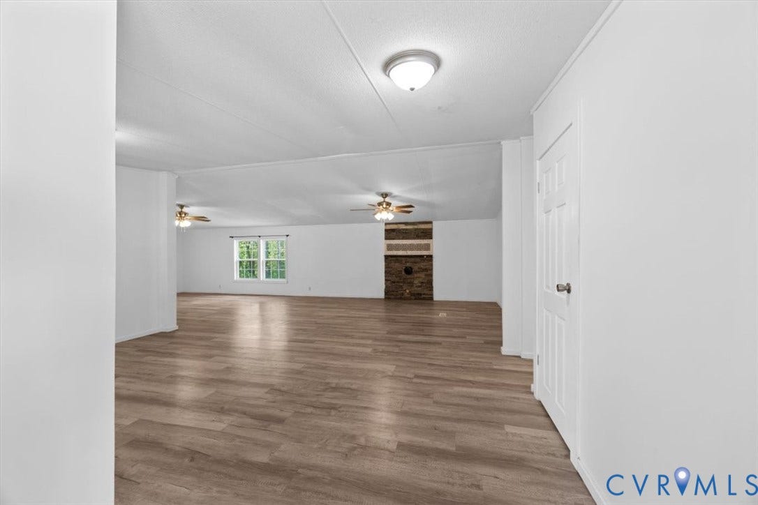 274 Frenchs Store Road, Cumberland, VA 23040 Open-concept interior featuring wood-finish flooring, a masonry fireplace, ceiling-mounted light fixtures, dual ceiling fans, and a six-panel door