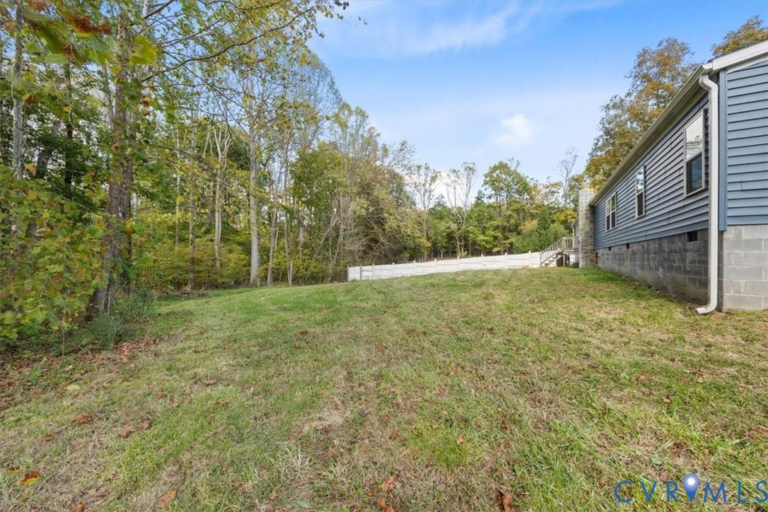 274 Frenchs Store Road, Cumberland, VA 23040 Rear exterior featuring horizontal lap siding, a concrete block foundation, and a white privacy fence bordering a wooded lot