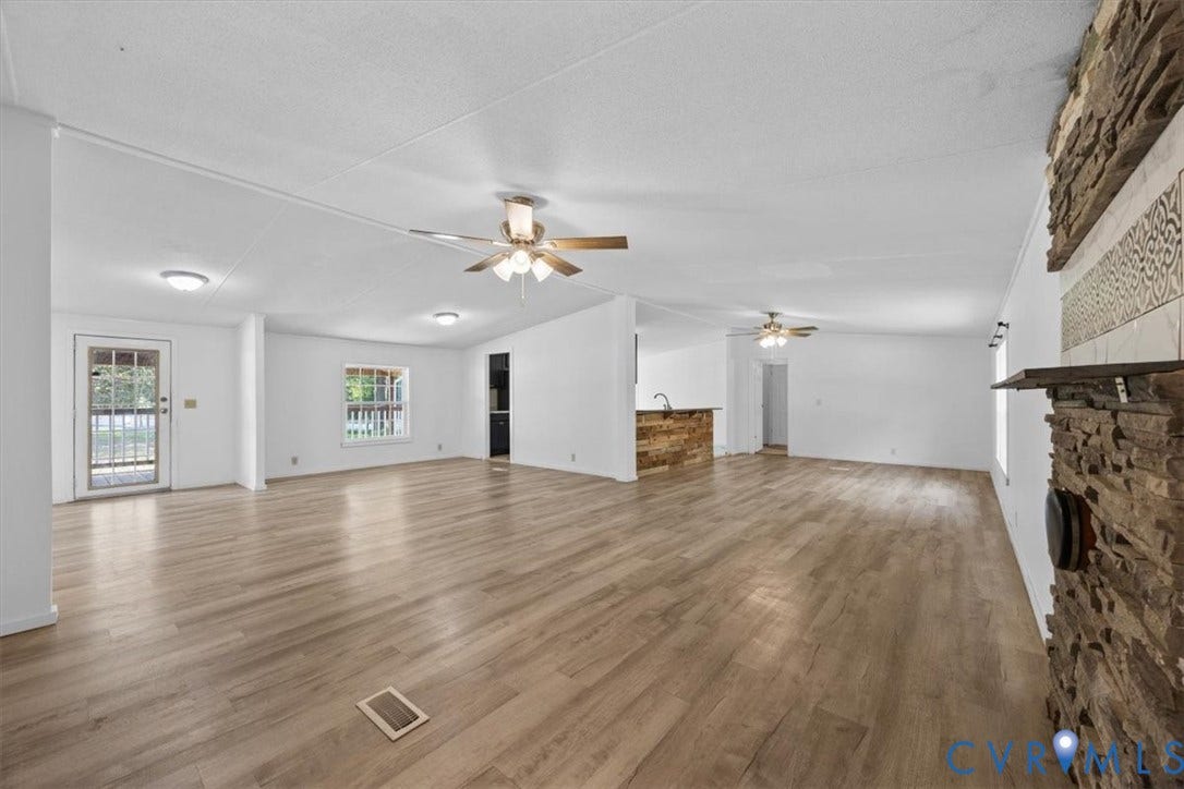 274 Frenchs Store Road, Cumberland, VA 23040 Open-concept interior featuring wood-finish flooring, a textured stone fireplace, dual ceiling fans, and a kitchen island with stone detailing