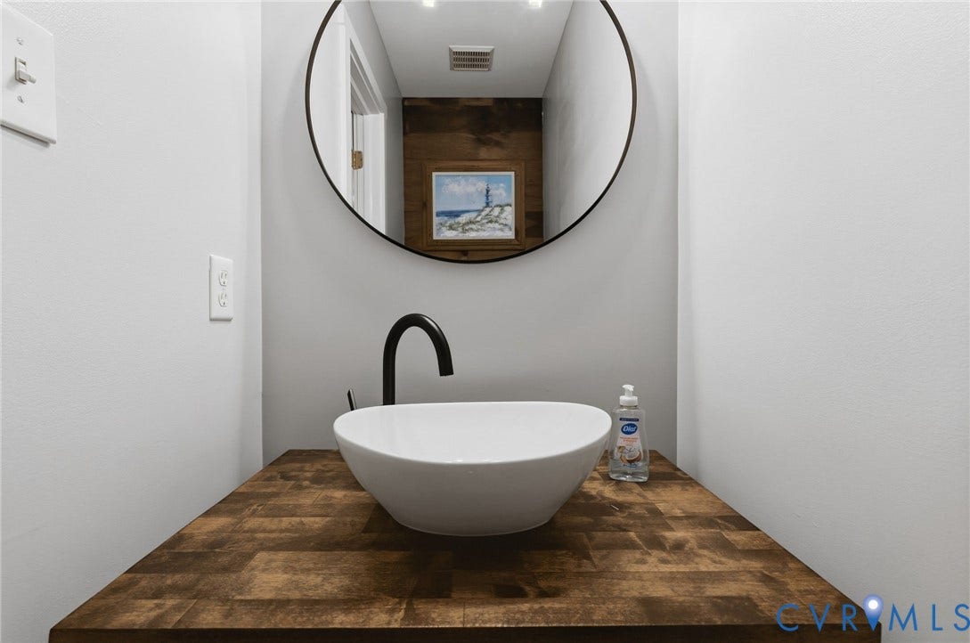 4350 Steger Creek Drive, Powhatan, VA 23139 Hardwood countertop with a white vessel sink, black wall-mounted faucet, and a round wall mirror