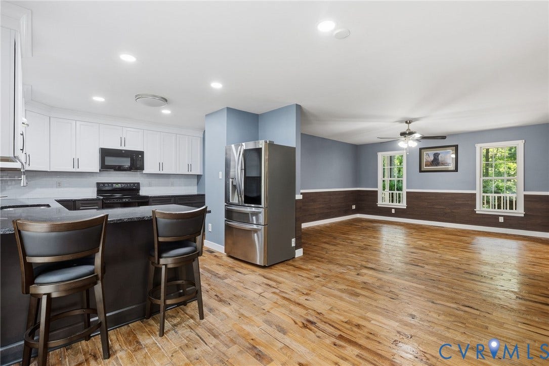 4350 Steger Creek Drive, Powhatan, VA 23139 Open-concept living space with wood-finish flooring, white upper cabinetry, and a dark-toned kitchen island with counter seating