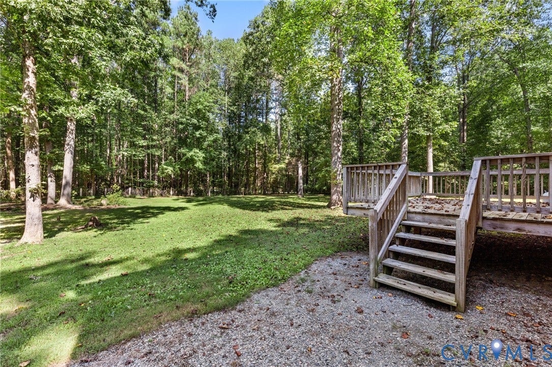 4350 Steger Creek Drive, Powhatan, VA 23139 Spacious wooden deck with railing, stairs, and gravel base, bordered by a substantial grassy area and mature trees