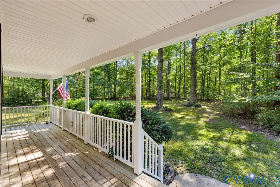 4350 Steger Creek Drive, Powhatan, VA 23139 Expansive covered porch featuring wood-finish decking and white railing, overlooking a lush green yard with mature trees