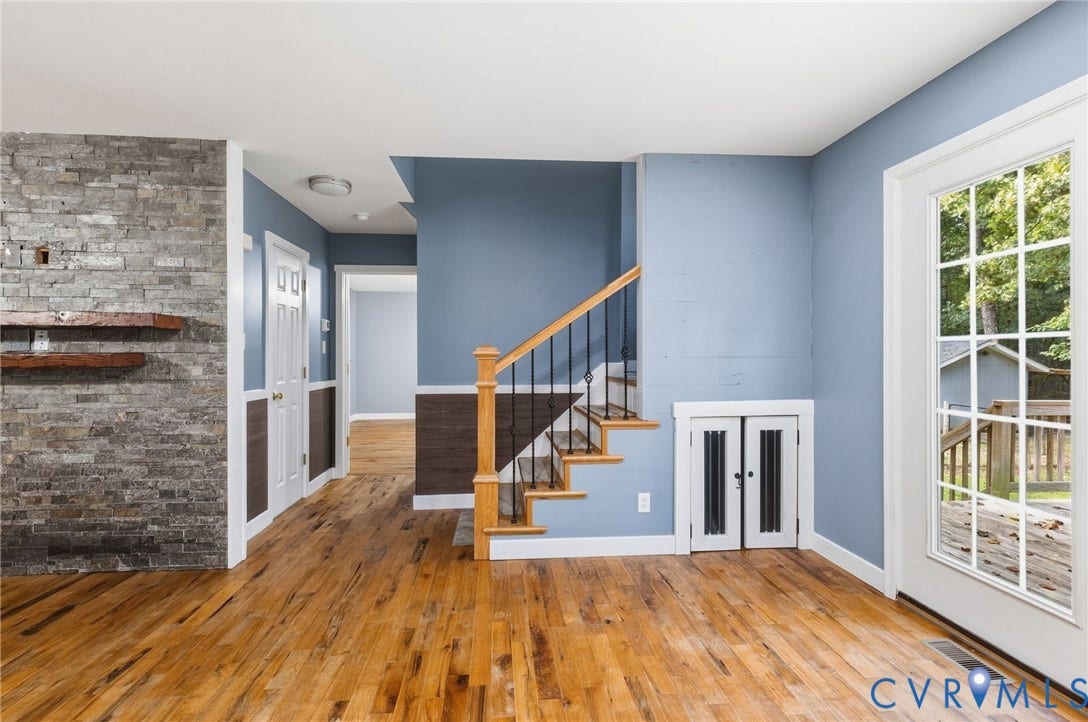4350 Steger Creek Drive, Powhatan, VA 23139 Hardwood flooring, stone accent wall with wood shelving, staircase with wood handrail and iron balusters, built-in storage under stairs, and French door with exterior deck access