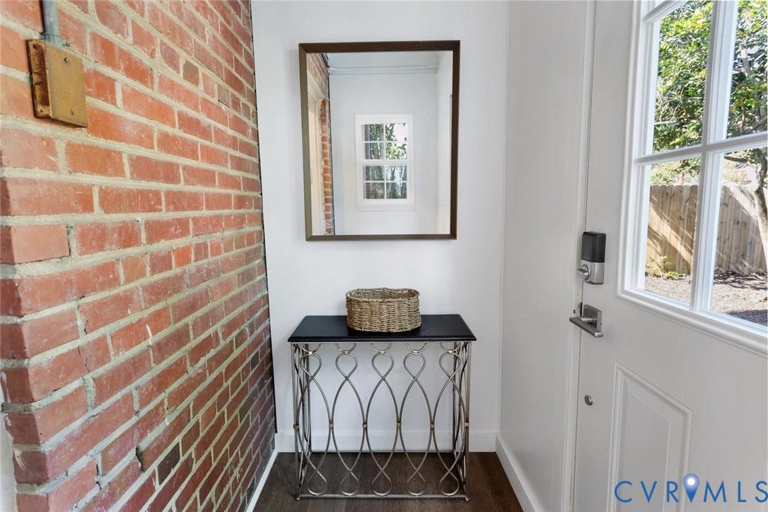 1316 Brookland Parkway, Richmond, VA 23227 Exposed brick wall, white paneled door with glass inserts, wood-finish flooring, wall-mounted mirror, and a decorative console table
