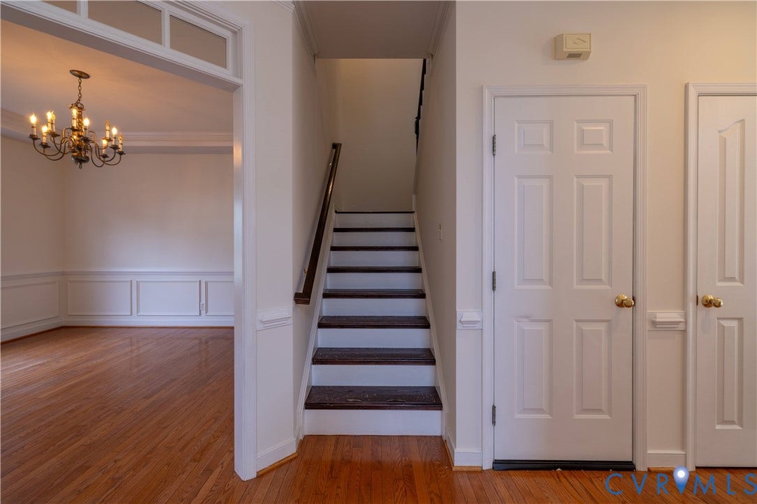 Hardwood flooring, classic chandelier, wainscoting, interior staircase with wood handrail, and paneled interior doors