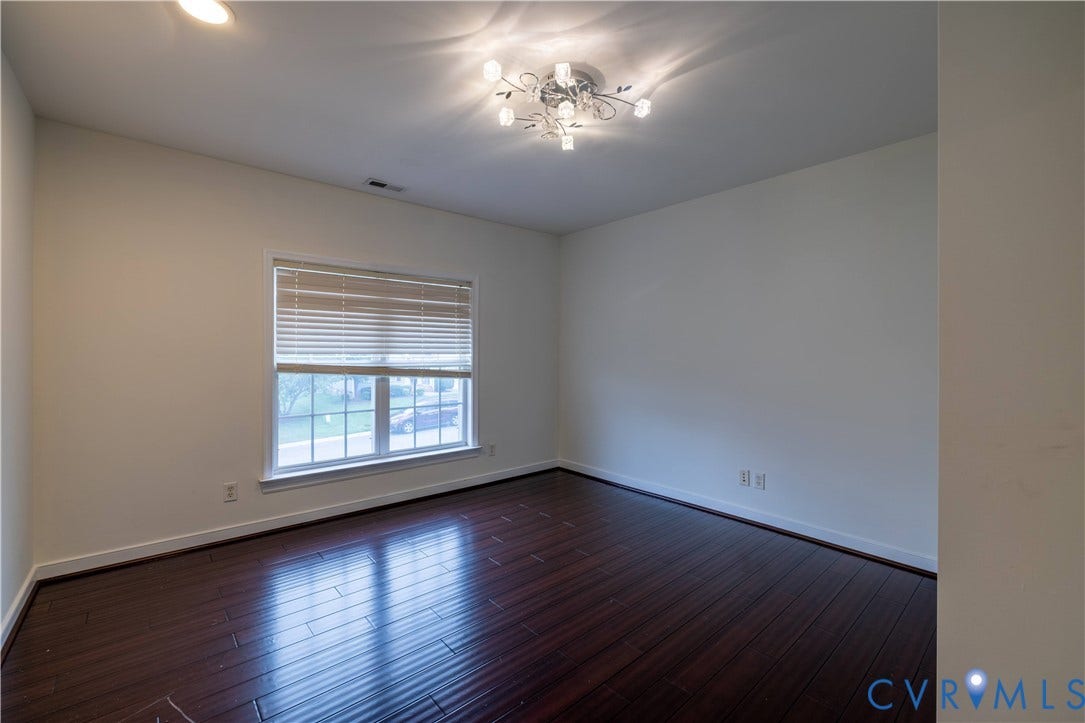 Rich wood-finish flooring, a large window with blinds, and a contemporary ceiling light fixture