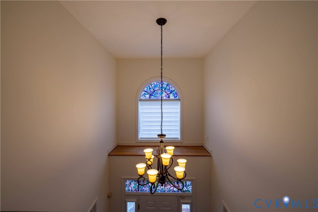 Two-story foyer with a chandelier, arched stained-glass window, and wood-finish ledge