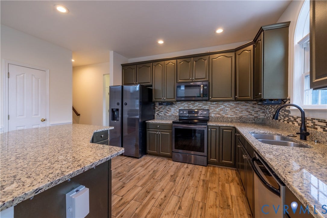 Kitchen featuring granite countertops, wood-finish flooring, dark cabinetry, stainless steel appliances, and a tiled backsplash