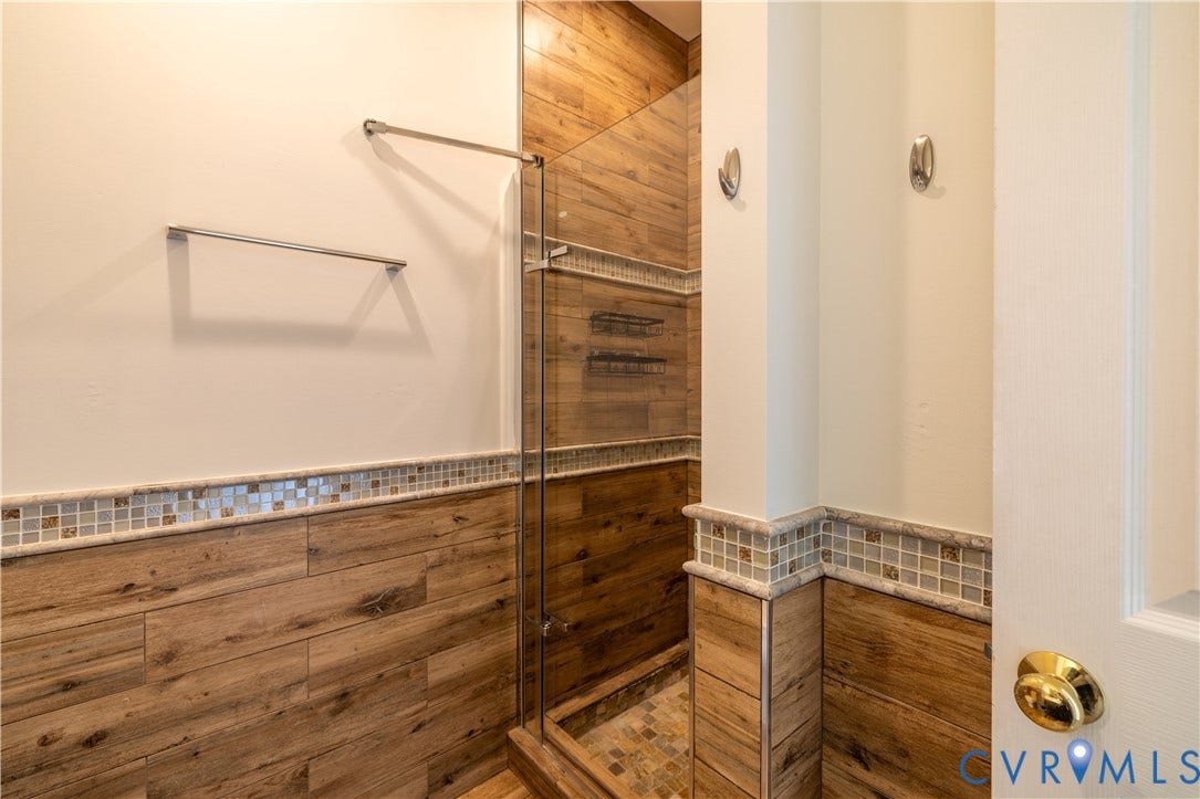 Shower enclosure featuring a frameless glass door, wood-look tile walls, and a mosaic tile accent band