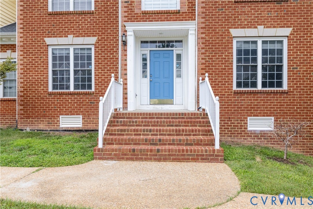 Brick facade with multiple windows, a blue front door, white doorframe, and brick front steps with white railings