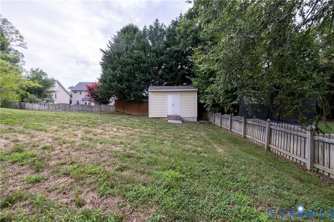 Spacious rear yard with a storage shed, mature trees, and a wood picket fence